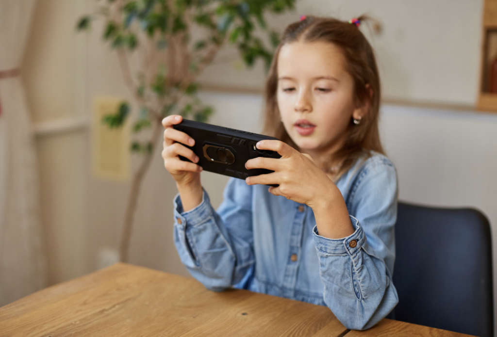 A child sits at a table, playing a game on a  cell phone